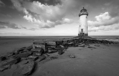 Lighthouse on beach by sea against sky