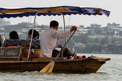 Rear view of man sitting on boat in city