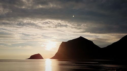 Silhouette mountain by sea against sky during sunset