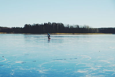 Person ice-skating on frozen lake against clear sky