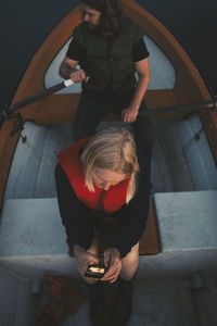 Woman using mobile phone while man rowing boat on lake