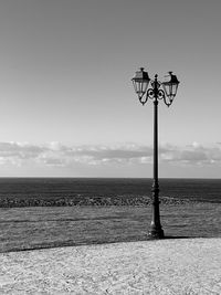 Street light on field by sea against sky