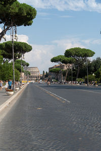 Road by trees in city against sky