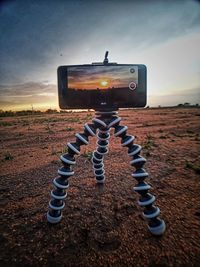 Close-up of camera on land against sky during sunset