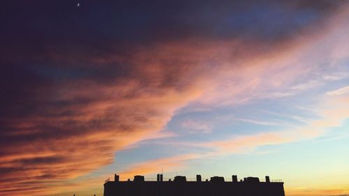 Silhouette of city against cloudy sky during sunset