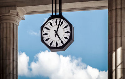 Clock hanging by columns against sky
