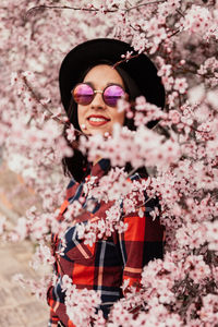Portrait of woman wearing sunglasses standing by cherry blossom