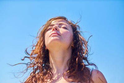 Low angle view of young woman with tousled hair against blue sky