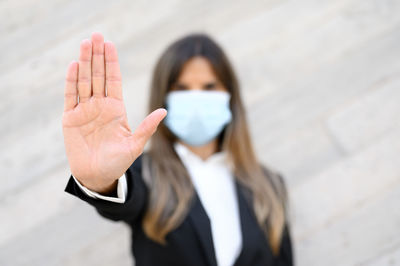 Portrait of businesswoman wearing mask gesturing while standing against wall
