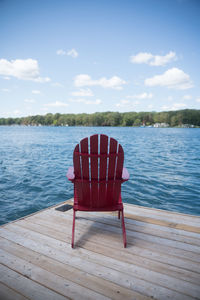 Empty chair on lake against sky