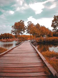 View of wooden walkway by lake against sky