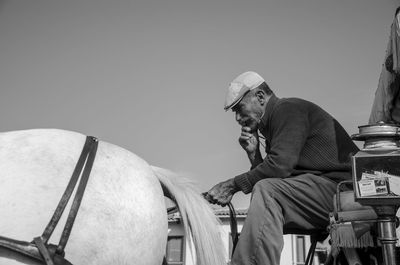 Low angle view of mature man riding horsecart against sky