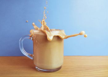 Close-up of coffee splashing from cup on wooden table against wall