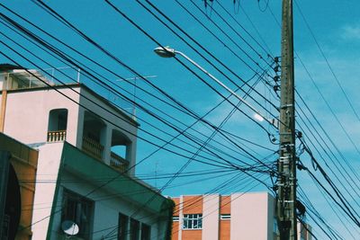 Low angle view of electricity pylon and buildings against blue sky