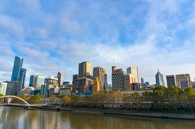 Buildings by river against sky in city