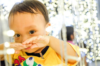 Close-up portrait of baby boy amidst illuminated christmas lights at night