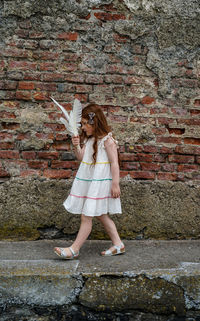 Young red head irish girl in pretty dress walking beside red brick wall 