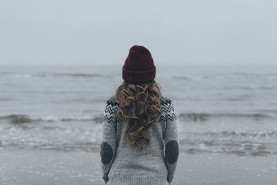 Rear view of woman standing at beach against sky