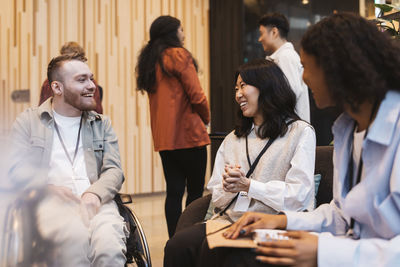 Smiling male entrepreneur with disability sitting next to businesswomen and discussing strategies at convention center