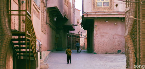 Rear view of people walking on narrow alley amidst buildings