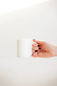 Midsection of woman holding coffee cup against white background