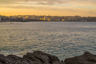 Sea by buildings against sky during sunset