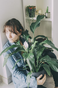 Young man looking at potted plant at home