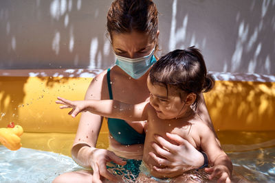 Young mother with a mask in an inflatable pool with her little daughter. safe holiday concept