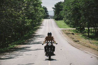 Man riding bicycle on road against trees