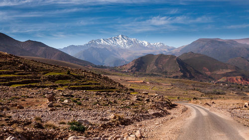 Dirt road by mountains against sky