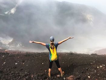 Rear view of young woman with arms outstretched standing on mountain during foggy weather