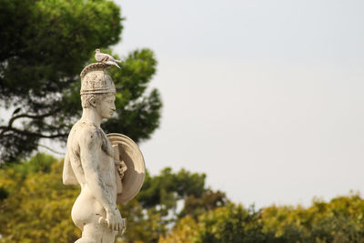 Statue against trees and plants against clear sky