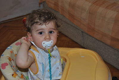 Portrait of cute baby boy sucking pacifier in walker at home