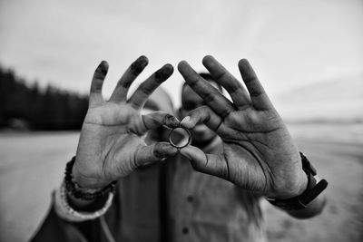 Man and woman holding ring at beach against sea and sky