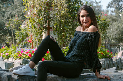 Portrait of smiling young woman sitting on rock in park