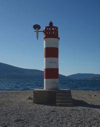 Lighthouse by sea against clear blue sky