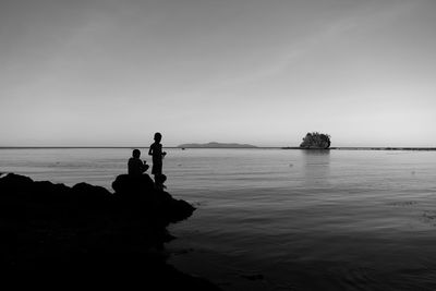 Silhouette people standing on rock by sea against sky