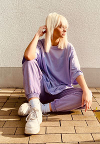 Full length of woman sitting on footpath against wall