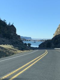 Empty road by mountain against clear sky