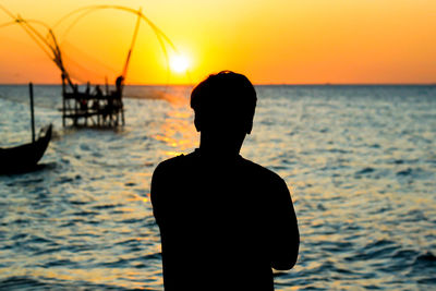 Rear view of silhouette man standing at beach during sunset