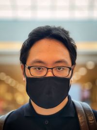 Close-up portrait of young man wearing eyeglasses and face mask against neon lights inside mall.