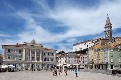 People on street by buildings in town against sky