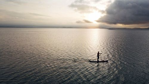 Silhouette man in sea against sky during sunset