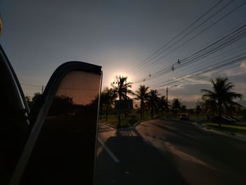 Cars on road by silhouette buildings against sky during sunset