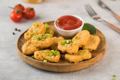 Golden chicken nuggets in a wooden plate, sprinkled with green onions and a lemon wedge. pub menu