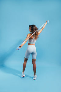 Rear view of woman exercising against blue background