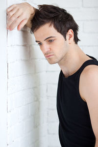 A 25-year-old man stands near a white wall.