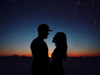 Silhouette romantic couple standing face to face on field against star field