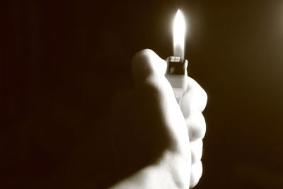 Close-up of hand holding lit candle in darkroom