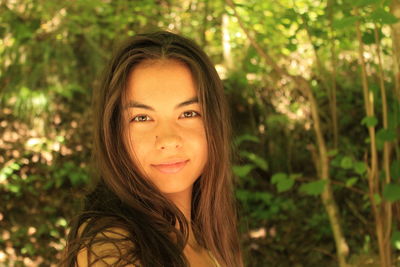 Portrait of smiling young woman with long hair standing against trees in forest
